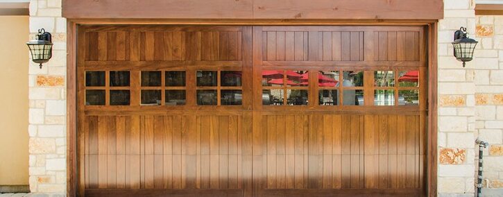 Wooden garage door with grid of small windows, set in a stone façade with two lantern-style lights.