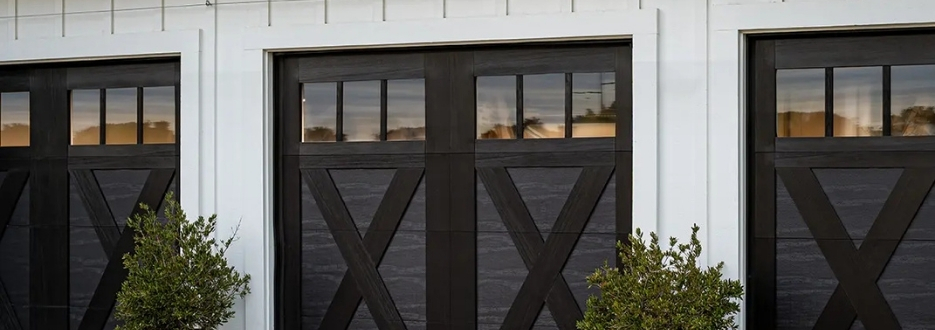 Garage Door Installation and Service by WD Door Omaha location Three black barn-style doors with X crossbars in a white building facade, with shrubs in front.